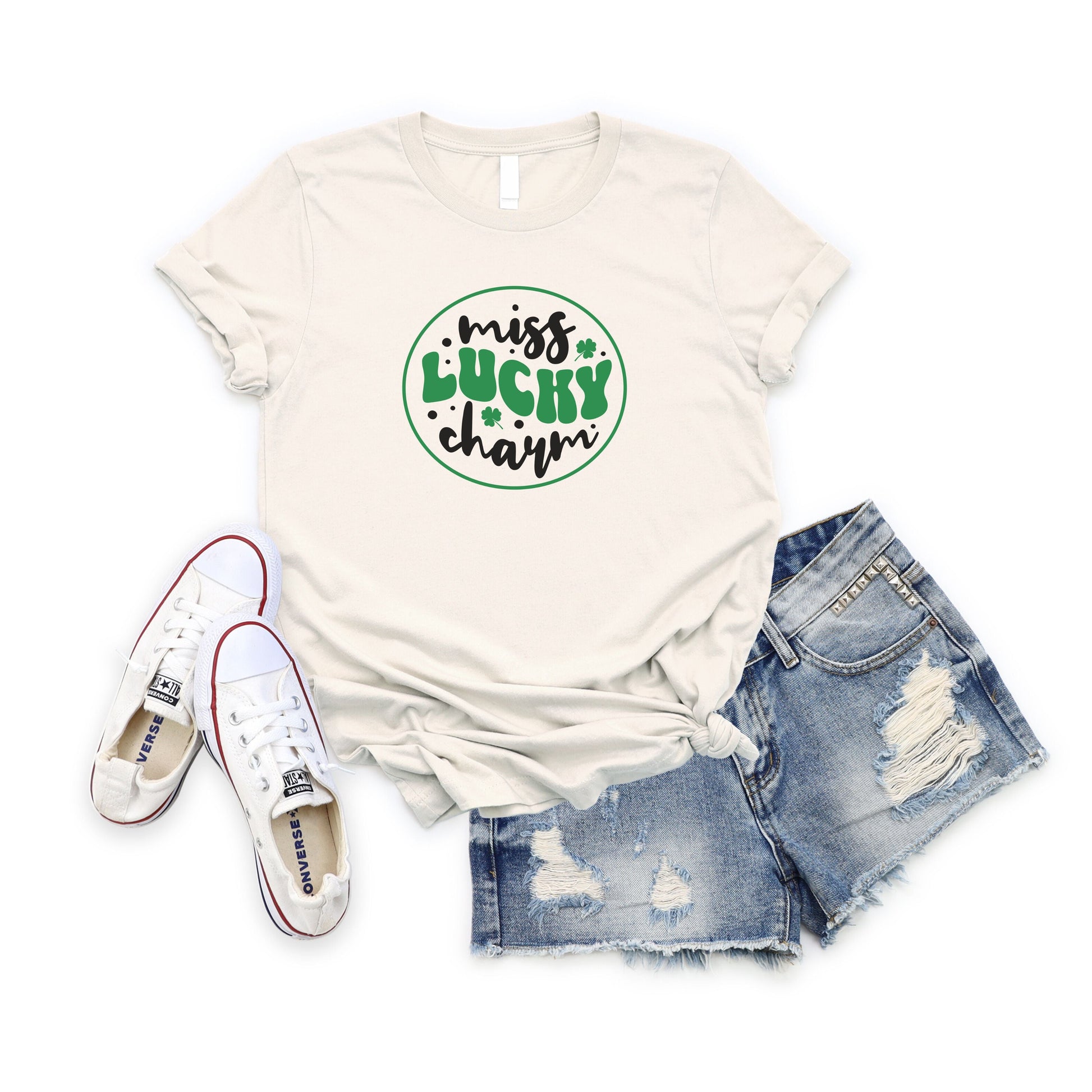 White Miss Lucky Charm T-shirt with green clover design paired with ripped denim shorts and white sneakers