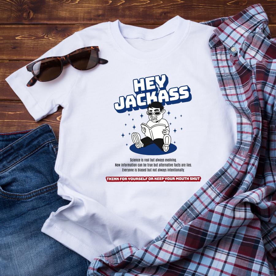 White Hey Jackass T-shirt with bold text and graphic of a person reading, styled with sunglasses, jeans, and a plaid shirt on a wooden background.