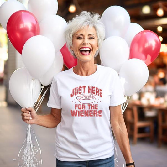 Woman wearing white Just Here for the Wieners T-Shirt holding red and white balloons and smiling
