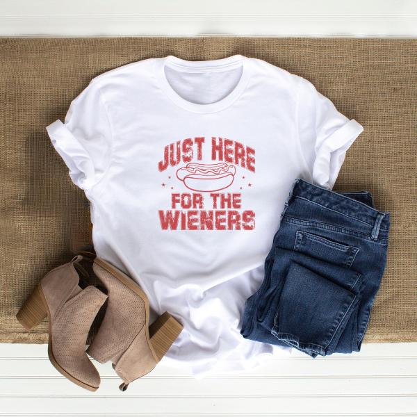 White Just Here for the Wieners T-Shirt with hot dog graphic, paired with blue jeans and beige ankle boots on a woven mat