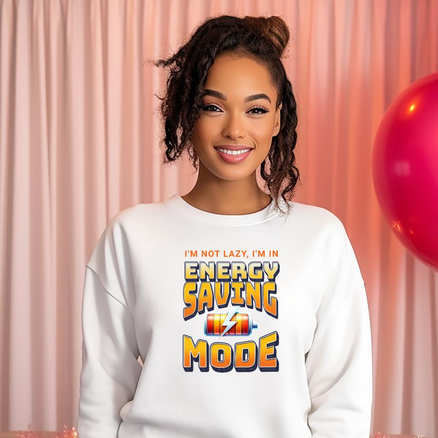 woman wearing white sweatshirt with "I'm not lazy, I'm in Energy Saving Mode" text design smiling in front of pink curtain background