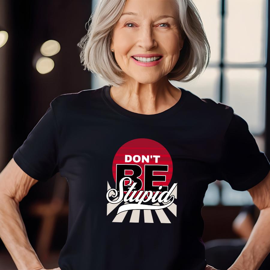 Older woman wearing a black "Don't Be Stupid" graphic t-shirt with red and white design smiling indoors
