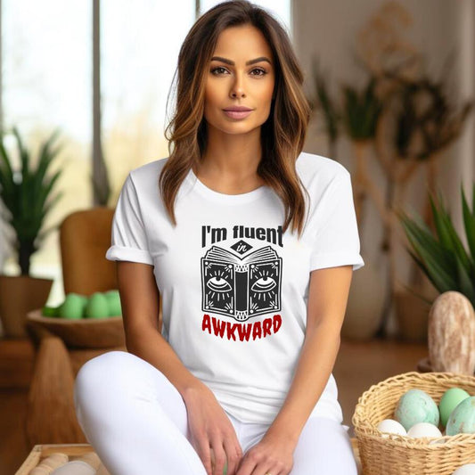 Woman wearing a white "I'm fluent in awkward" graphic t-shirt sitting indoors with plants and a basket of pastel Easter eggs nearby