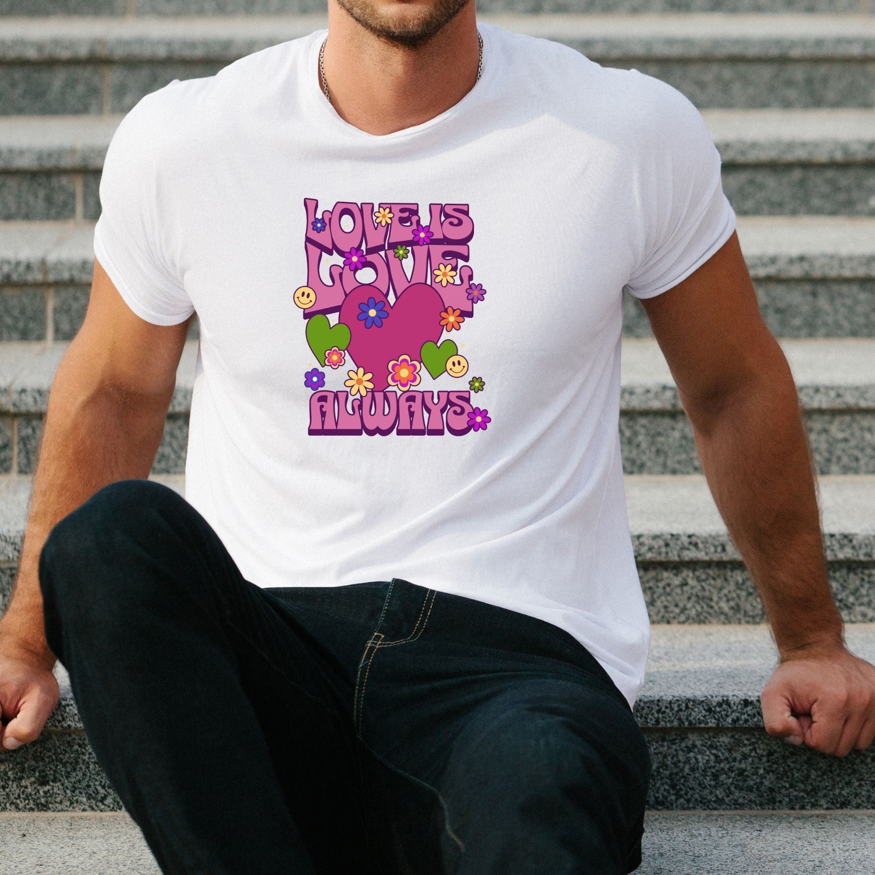 White t-shirt with colorful "Love is Love Always" graphic featuring hearts and flowers, worn by seated man.