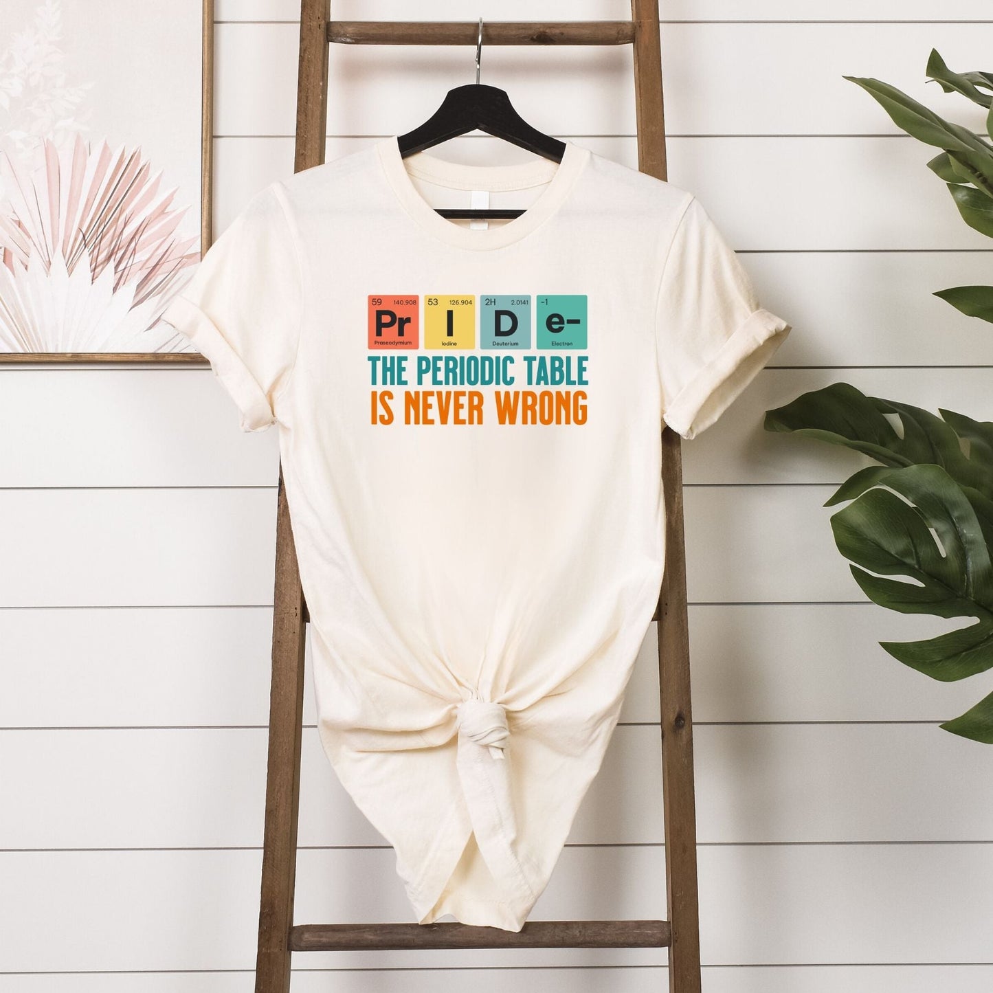 The Periodic Table is Never Wrong T-shirt with PRIDE spelled using periodic table elements, tied front white tee displayed on wooden ladder with plants background