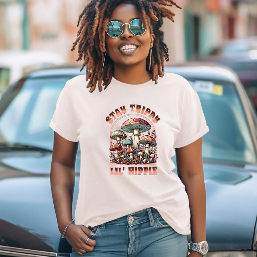 Stay Trippy Lil' Hippie T-shirt with colorful psychedelic mushroom design worn by smiling woman with sunglasses