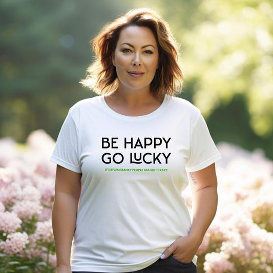 Woman wearing white Be Happy Go Lucky graphic t-shirt outdoors with greenery background
